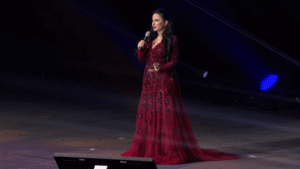 Cryptoqueen Ruja Ignatova in red gown, addressing followers at the OneCoin marketing event.