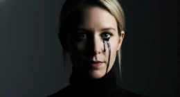 A cinematic close-up of Elizabeth Holmes, portraying the Theranos fraud. Her face is half in shadow, and a single black tear is running from her eye.