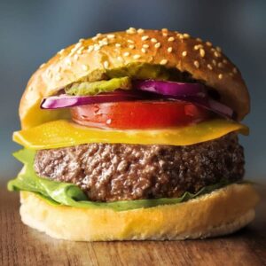 A complete cheeseburger with lettuce, tomato, cheese, and red onion on a sesame seed bun.
