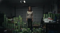 A distressed woman stands in a garage filled with stacks of unsold "Herbalife MLM" products, symbolizing the financial loss and inventory loading.